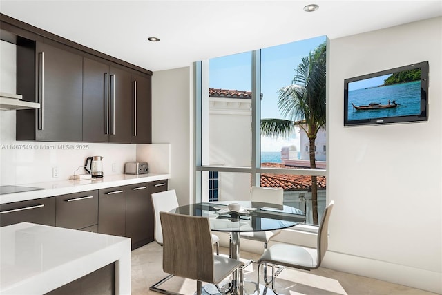 kitchen featuring expansive windows, black electric cooktop, wall chimney exhaust hood, and dark brown cabinets