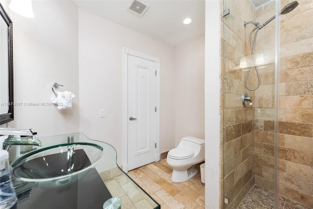 bathroom with hardwood / wood-style floors, toilet, sink, and tiled shower