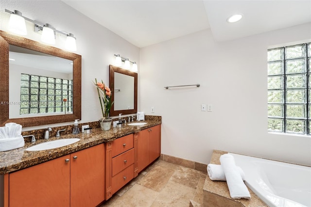 bathroom with a washtub, dual bowl vanity, and a wealth of natural light