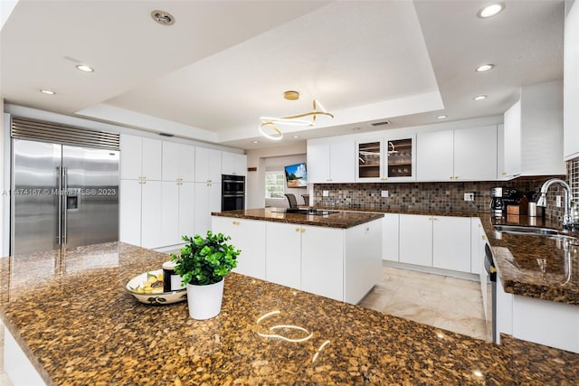 kitchen featuring stainless steel built in fridge, a kitchen island, dark stone counters, tasteful backsplash, and sink