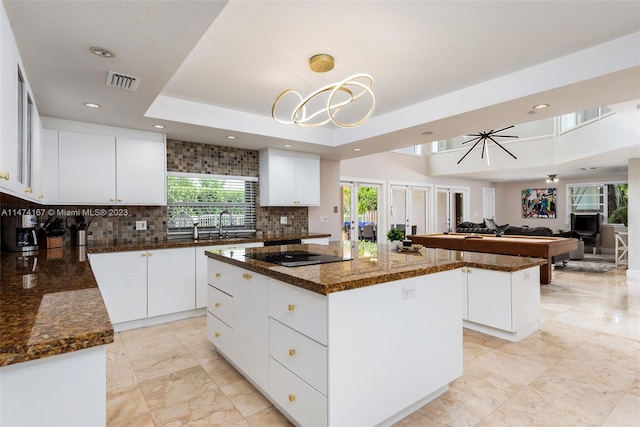 kitchen featuring decorative light fixtures, white cabinetry, a tray ceiling, a kitchen island, and tasteful backsplash