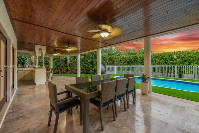 patio terrace at dusk featuring ceiling fan and a fenced in pool