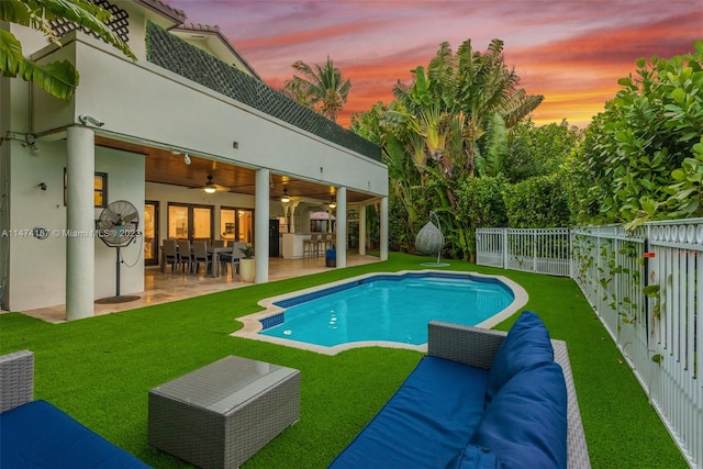 pool at dusk with a patio area, an outdoor living space, ceiling fan, and a yard