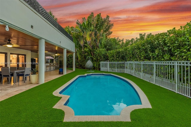 pool at dusk with a yard, a patio area, and ceiling fan