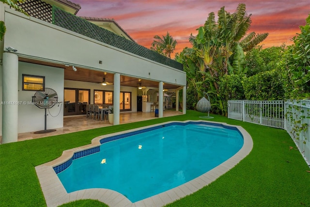 pool at dusk with a lawn, ceiling fan, and a patio