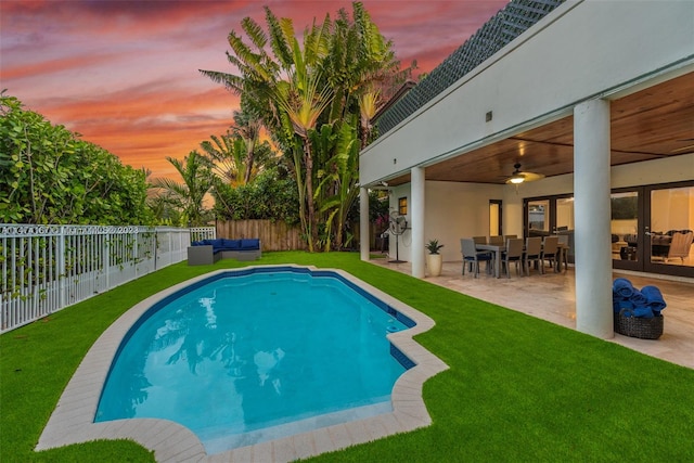 pool at dusk featuring ceiling fan, a lawn, and a patio area