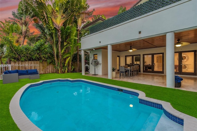 pool at dusk featuring a lawn, ceiling fan, and a patio