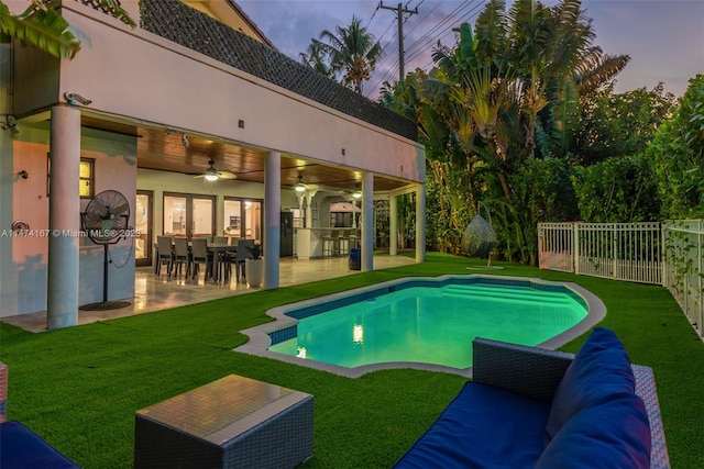 pool at dusk featuring an outdoor hangout area, a yard, ceiling fan, and a patio area