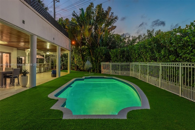 pool at dusk with a patio area, a lawn, and ceiling fan