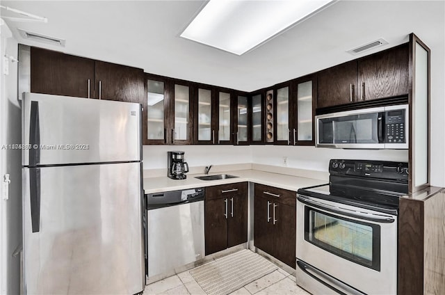 kitchen featuring light tile flooring, dark brown cabinetry, stainless steel appliances, and sink