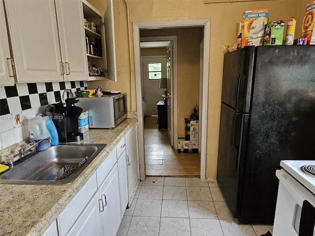 kitchen featuring light hardwood / wood-style floors, white stove, sink, white cabinetry, and black refrigerator