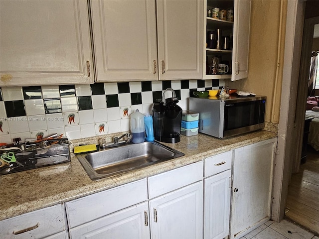 kitchen with light tile patterned flooring, sink, tasteful backsplash, and white cabinetry