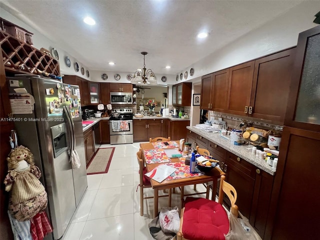 kitchen with a notable chandelier, stainless steel appliances, light tile floors, dark brown cabinets, and pendant lighting