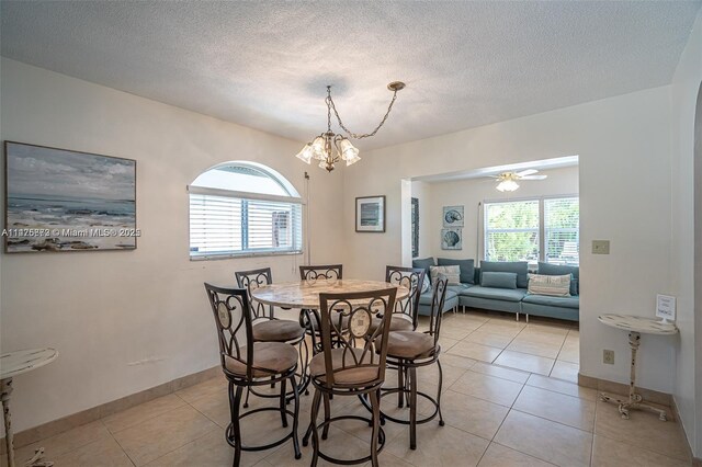 tiled dining area featuring a textured ceiling and ceiling fan with notable chandelier