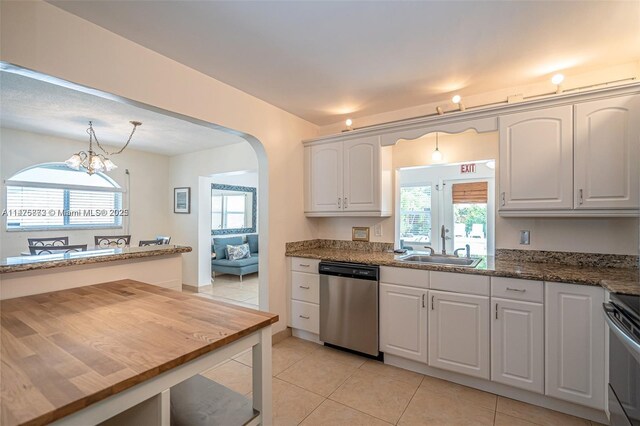 kitchen featuring stainless steel dishwasher, light tile floors, a notable chandelier, dark stone counters, and white cabinetry