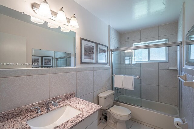 full bathroom featuring tile walls, toilet, tile floors, combined bath / shower with glass door, and vanity