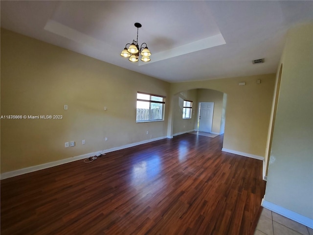 empty room with a raised ceiling, hardwood / wood-style floors, and a chandelier