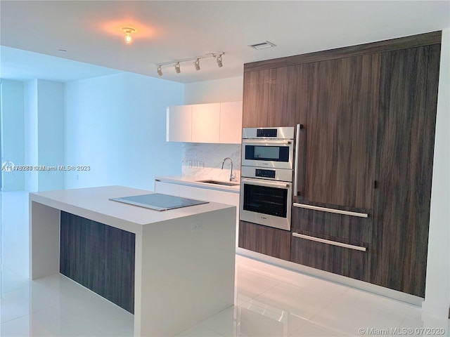 kitchen featuring light tile flooring, rail lighting, white cabinets, stainless steel double oven, and sink