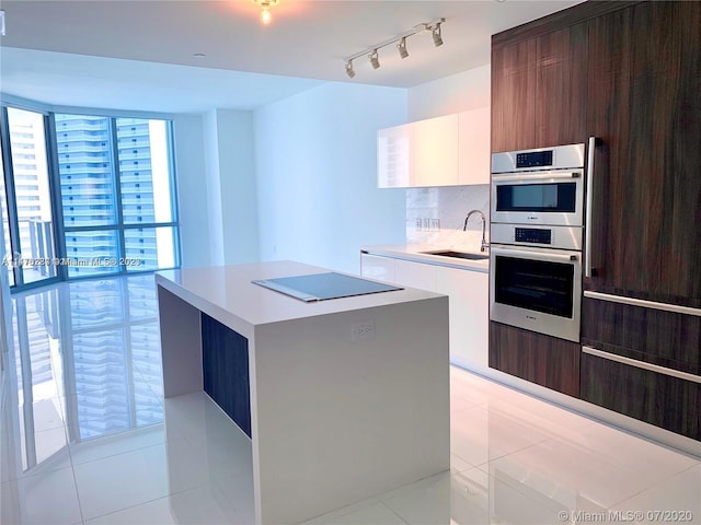 kitchen with a center island, white cabinetry, stainless steel double oven, track lighting, and sink