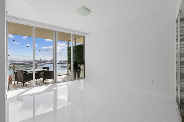 tiled empty room featuring a water view and a wall of windows