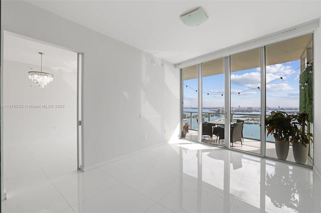 empty room with a chandelier, a water view, light tile floors, and a wall of windows