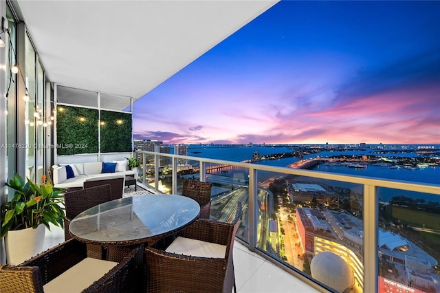 balcony at dusk featuring a water view and outdoor lounge area