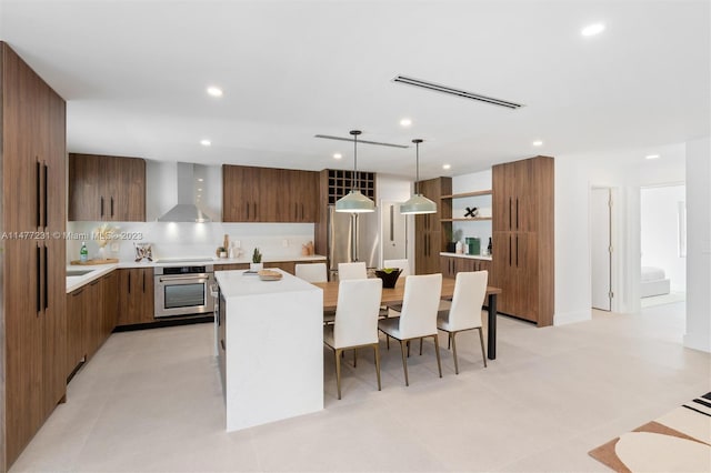 kitchen with pendant lighting, wall chimney exhaust hood, light tile patterned flooring, a center island, and stainless steel appliances