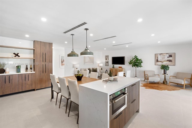 kitchen featuring oven, light tile patterned floors, a kitchen island, a kitchen bar, and decorative light fixtures