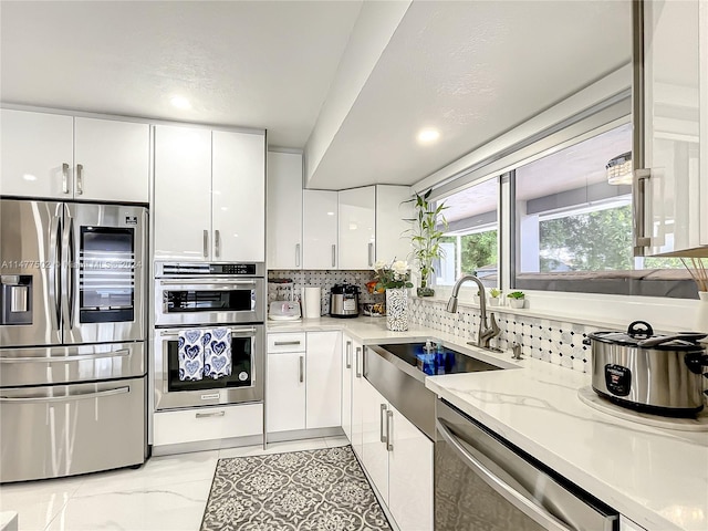 kitchen with light tile floors, light stone counters, white cabinets, appliances with stainless steel finishes, and backsplash