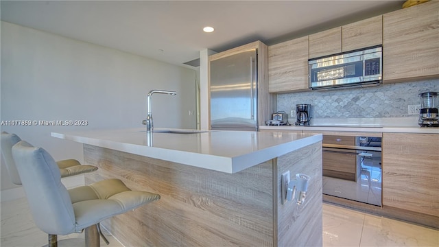 kitchen featuring sink, light tile floors, black appliances, tasteful backsplash, and a kitchen bar