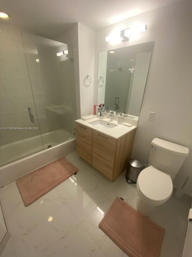 full bathroom featuring combined bath / shower with glass door, tile floors, vanity with extensive cabinet space, and toilet