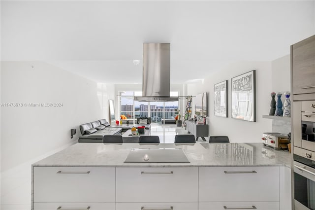 kitchen with black electric cooktop, island range hood, wall oven, oven, and light stone counters