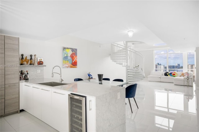 kitchen featuring light stone countertops, kitchen peninsula, wine cooler, sink, and light tile floors