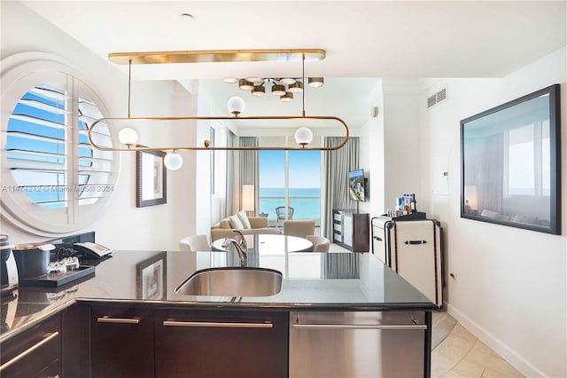 kitchen with sink, a water view, light tile floors, dark brown cabinetry, and pendant lighting