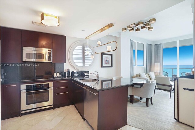 kitchen with pendant lighting, sink, dark brown cabinets, stainless steel appliances, and a water view