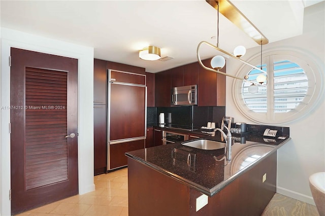 kitchen featuring kitchen peninsula, sink, dark stone countertops, paneled built in refrigerator, and pendant lighting