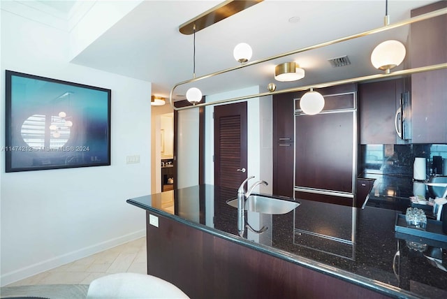 kitchen featuring pendant lighting, light tile floors, backsplash, dark stone countertops, and sink