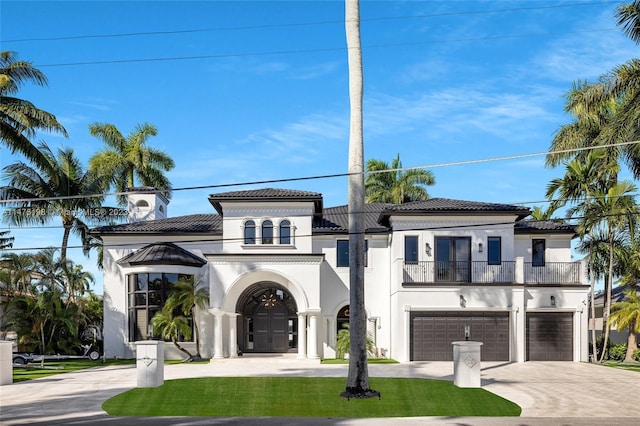 mediterranean / spanish-style house with an attached garage, a balcony, driveway, a tiled roof, and stucco siding