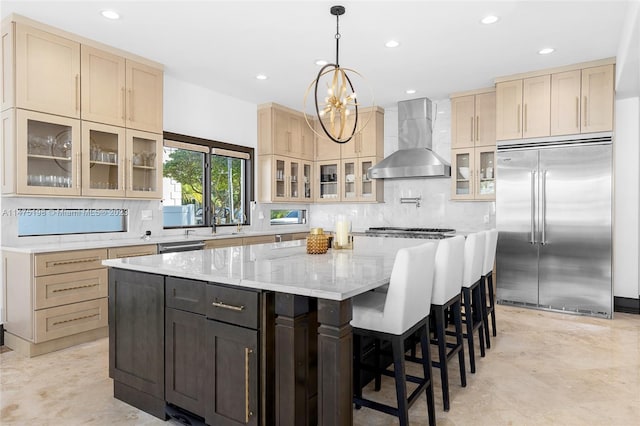 kitchen featuring light stone counters, a kitchen island, appliances with stainless steel finishes, wall chimney range hood, and pendant lighting