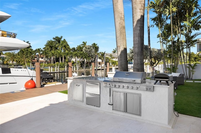 view of patio with area for grilling, fence, an outdoor kitchen, and a water view