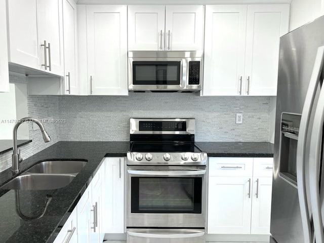 kitchen featuring white cabinets, sink, stainless steel appliances, and dark stone counters