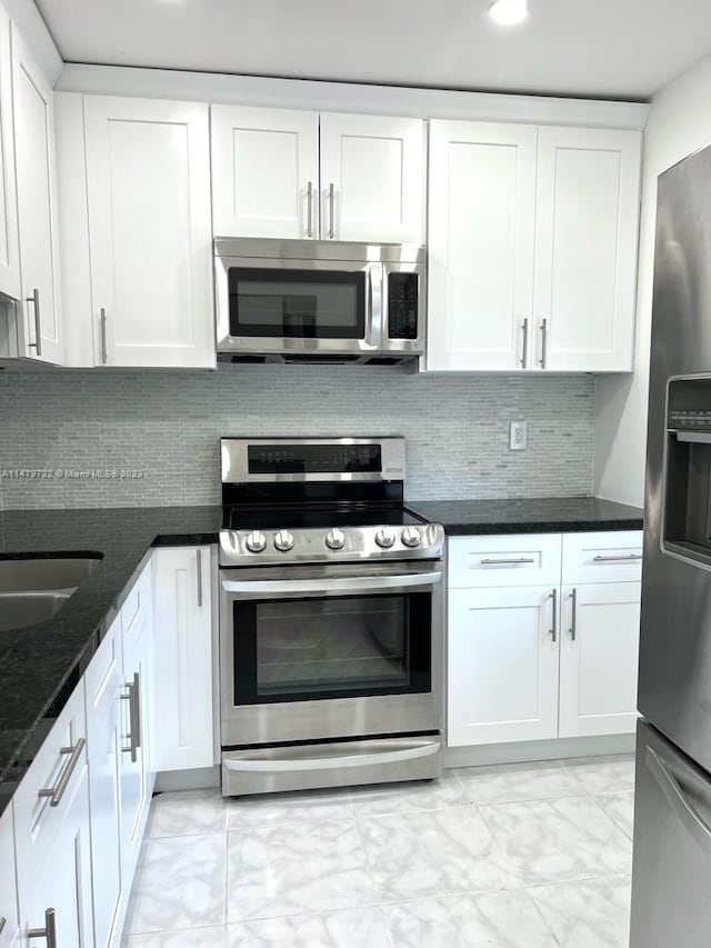 kitchen featuring backsplash, dark stone counters, white cabinets, sink, and appliances with stainless steel finishes