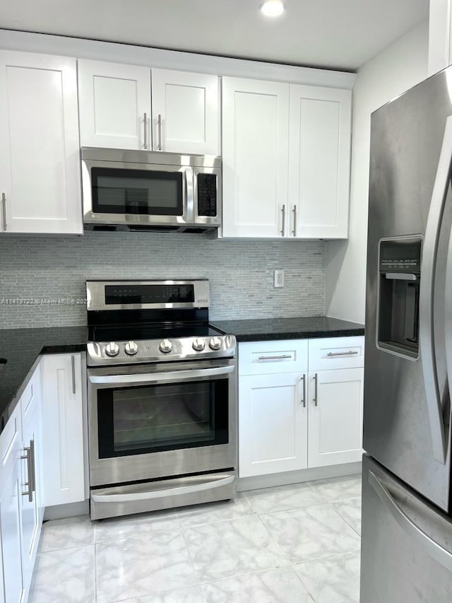 kitchen with tasteful backsplash, dark stone countertops, white cabinets, and appliances with stainless steel finishes