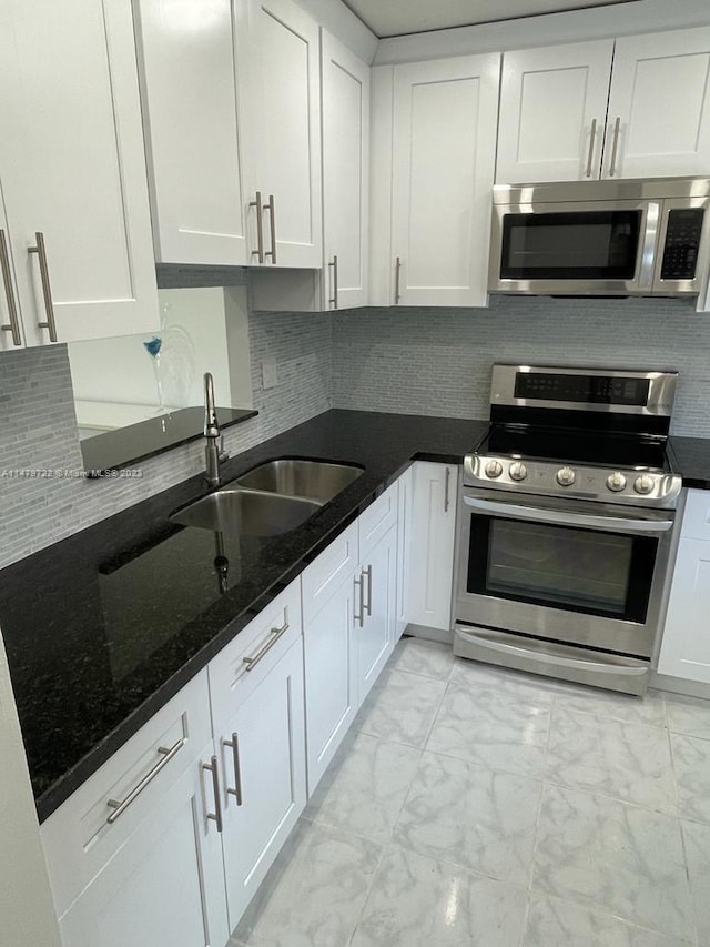 kitchen featuring sink, tasteful backsplash, dark stone countertops, white cabinets, and appliances with stainless steel finishes