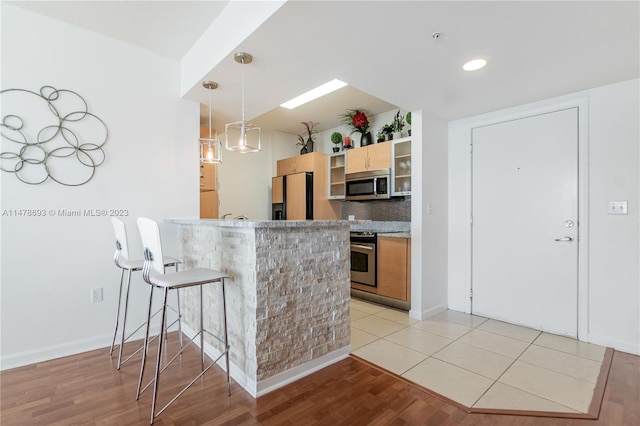 2775 NE 187th St Unit 516, Aventura, FL 33180 - kitchen featuring stainless steel appliances, light wood-style floors, a kitchen breakfast bar, tasteful backsplash, and a peninsula