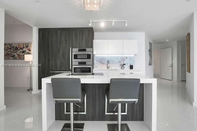 kitchen with white cabinetry, double oven, an inviting chandelier, a breakfast bar, and track lighting