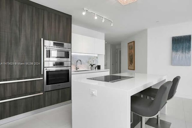 kitchen with double oven, a kitchen bar, black electric stovetop, white cabinets, and sink