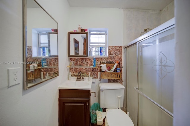 bathroom with backsplash, toilet, vanity with extensive cabinet space, and a shower with shower door