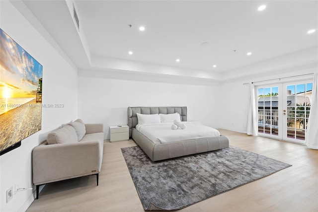 bedroom with french doors, a tray ceiling, access to exterior, and light hardwood / wood-style flooring