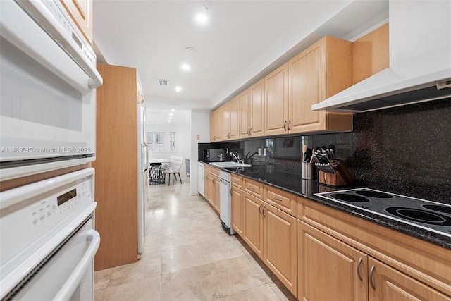 kitchen featuring white appliances, light tile floors, dark stone countertops, tasteful backsplash, and wall chimney exhaust hood